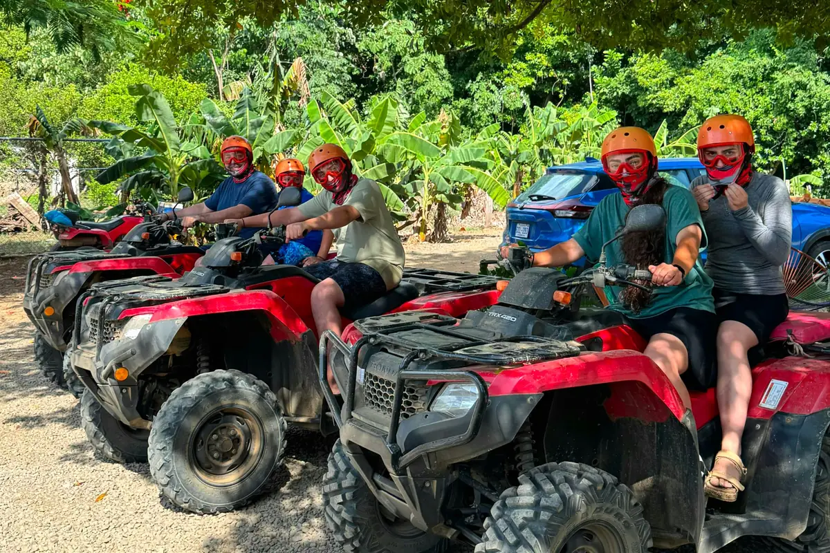 A group of riders in helmets and goggles lined up on red Honda ATVs before a tour near Playas del Coco