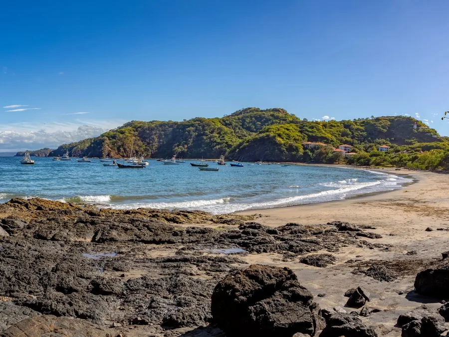 Rocky cove and sandy beach with boats anchored in a calm bay on the Guanacaste coast
