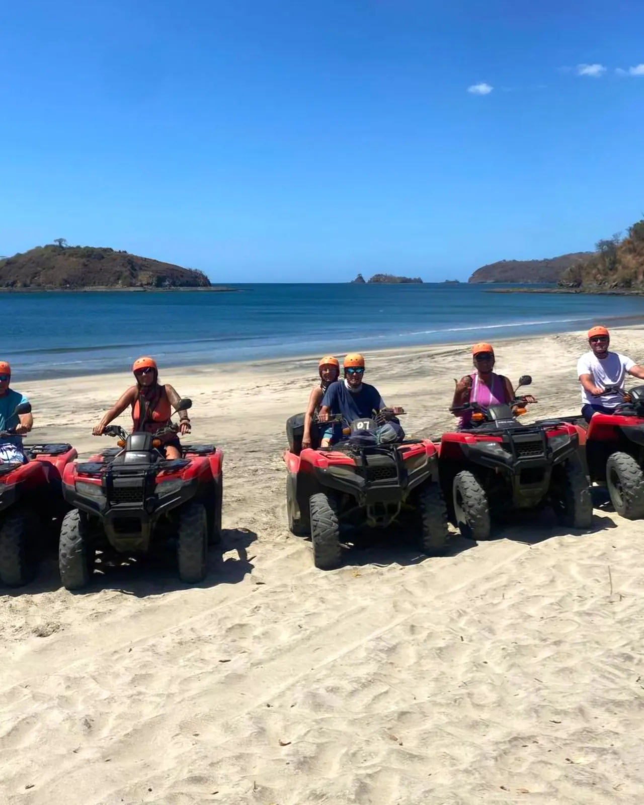Riders in orange helmets on red Honda ATVs lined up on a Guanacaste beach before snorkeling