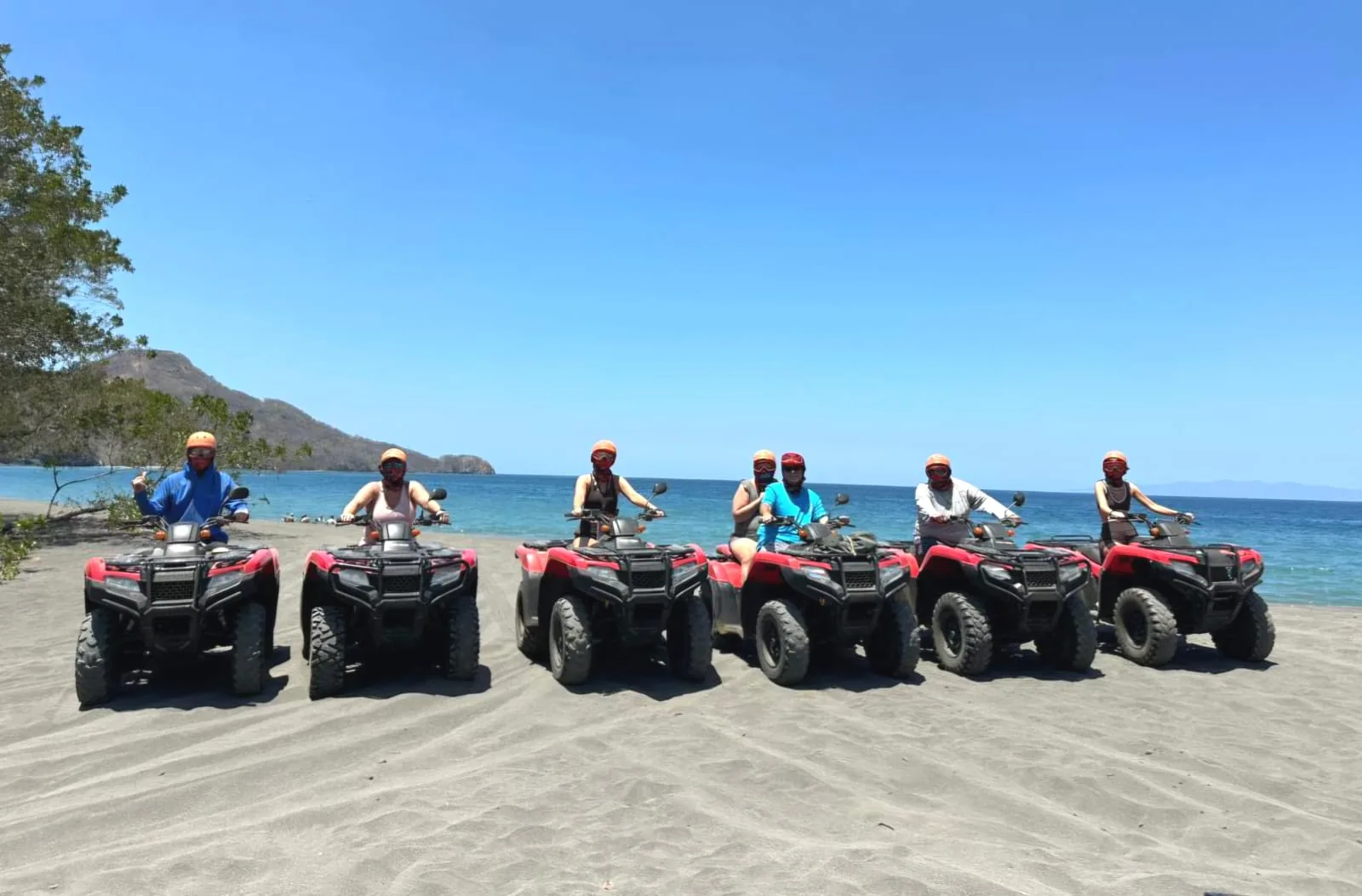 Seven riders in helmets lined up on red Honda ATVs on a beach near Playas del Coco, Costa Rica