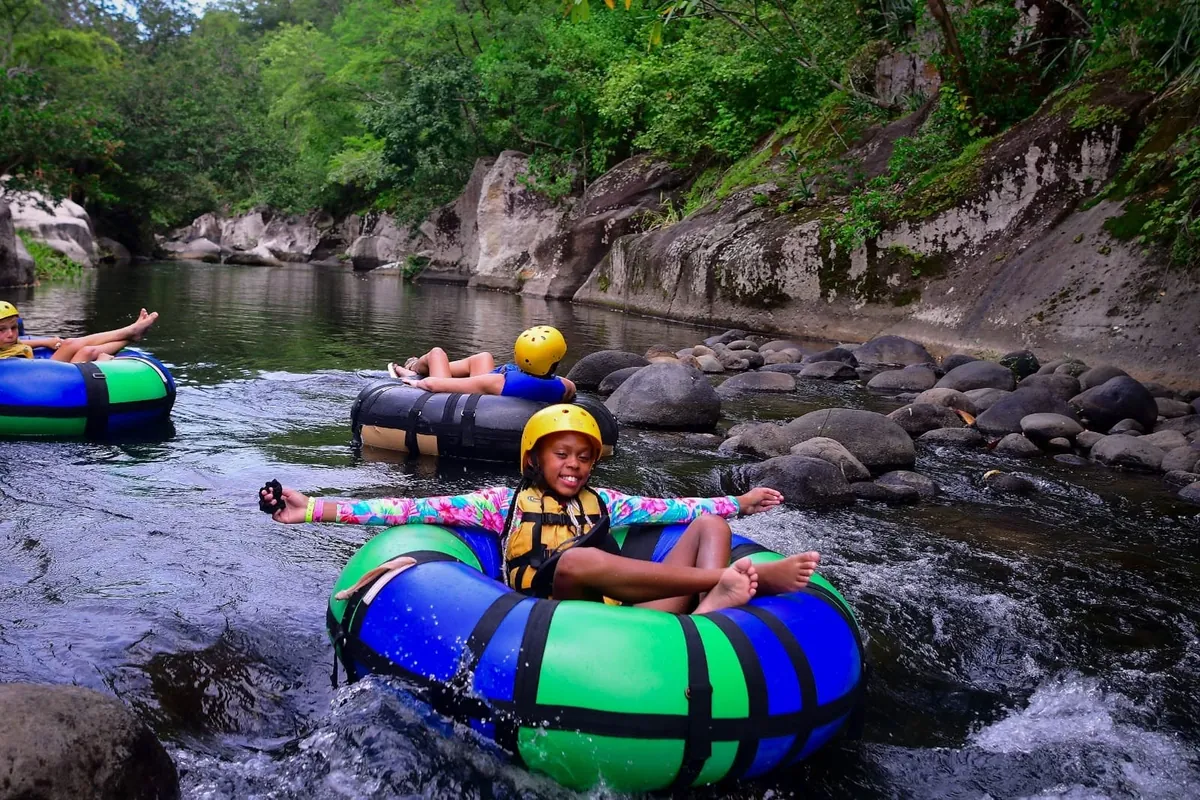 Smiling girl in a helmet and life jacket river tubing with arms outstretched on the Rio Colorado at Cañon de la Vieja