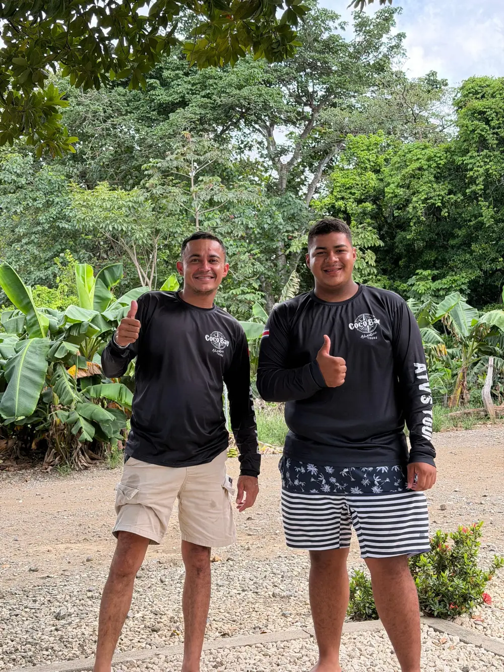 Two Coco ATV Tours guides giving a thumbs up in front of tropical trees at the ATV base in Guanacaste, Costa Rica
