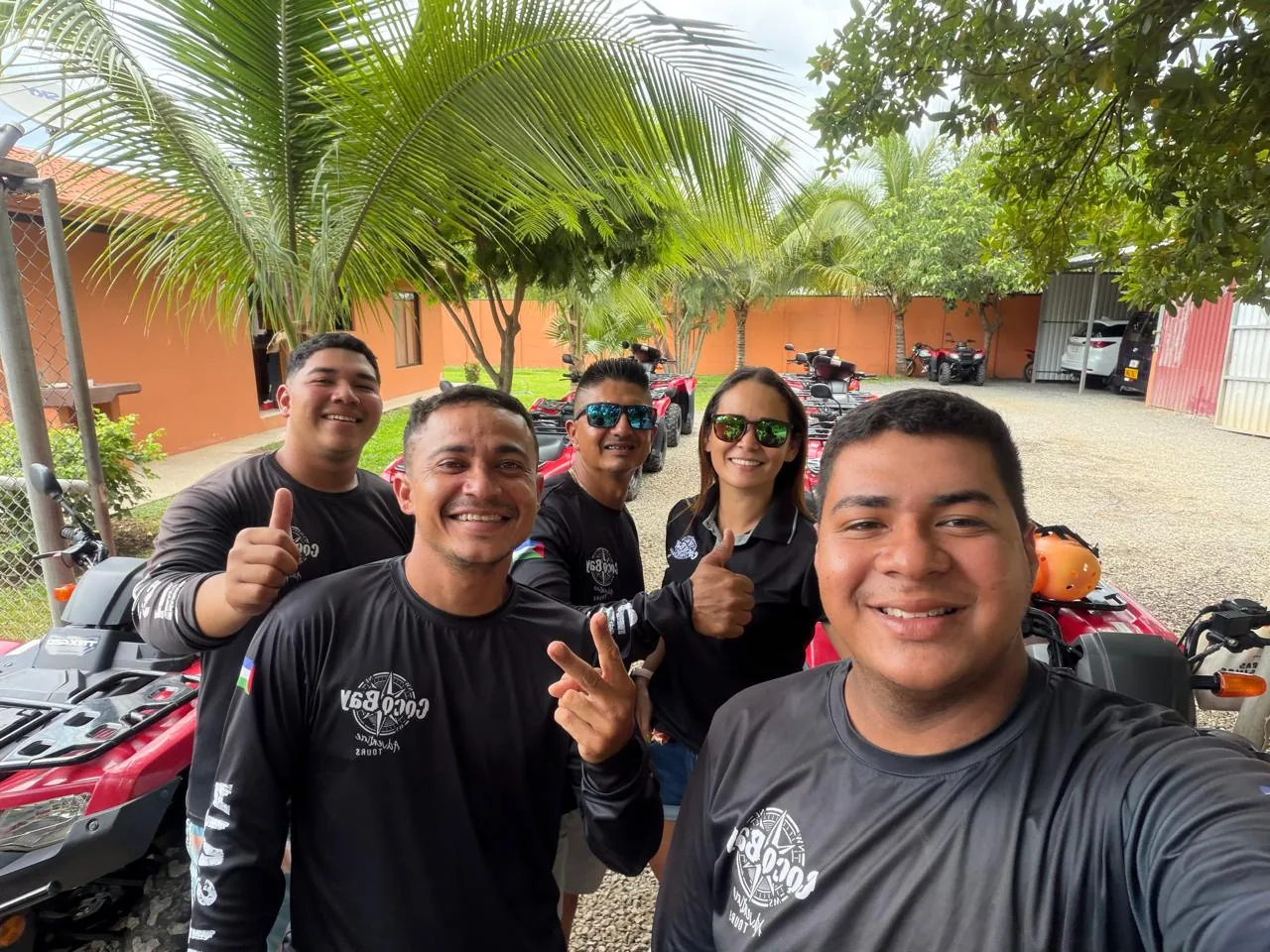 Coco ATV Tours team smiling with thumbs up in front of their red ATVs at the tour base in Playas del Coco, Costa Rica
