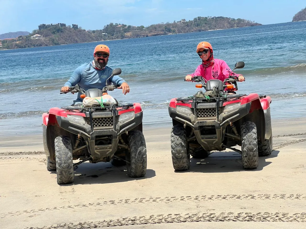 Two riders in helmets on red Honda ATVs on a beach near Playas del Coco, Costa Rica