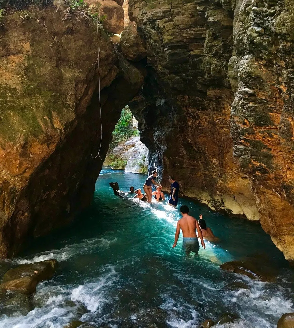 Group wading through turquoise water under a natural rock arch in the La Leona canyon