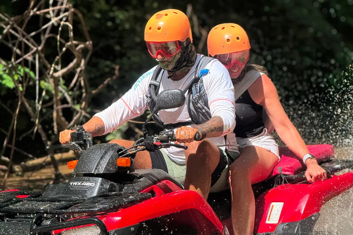 Couple on a red Honda ATV splashing through a river crossing on a mountain jungle tour in Guanacaste