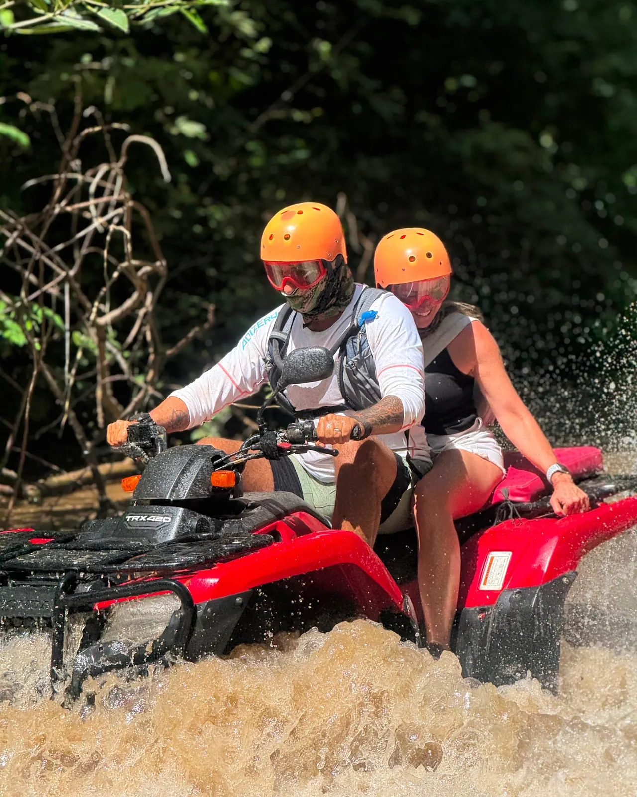 Couple on a red Honda ATV splashing through a river crossing on a mountain jungle tour in Guanacaste