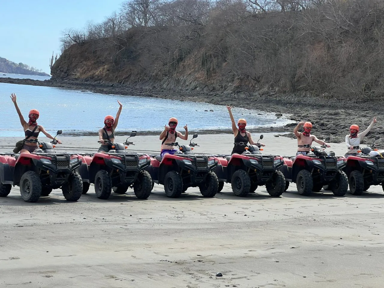 A group of six riders raising their arms on red ATVs on a beach near Playas del Coco, Costa Rica
