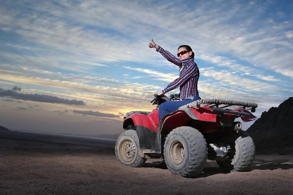 Rider giving a thumbs-up from a red ATV under a golden-hour sky