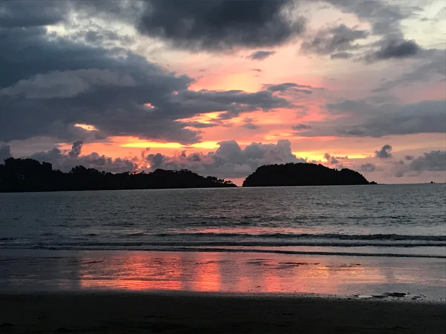 Pink and orange sunset clouds over island silhouettes, reflected on a wet beach on the Guanacaste coast