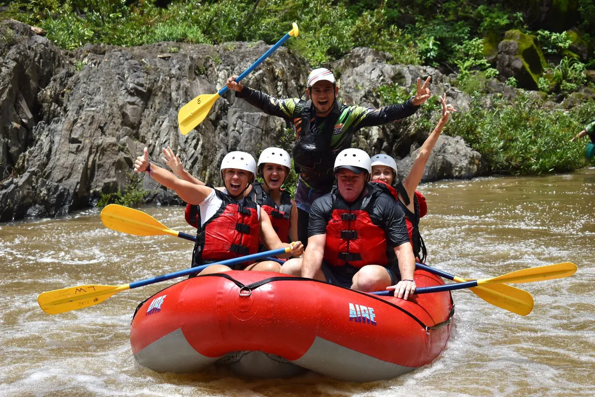 Guests and rafting guide cheering in a red raft on the Tenorio River during a tour from Playas del Coco