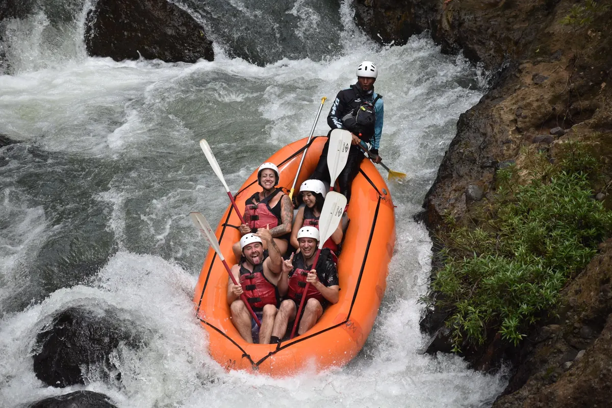 Guide and rafters in an orange raft dropping through whitewater rapids on the Tenorio River in Guanacaste