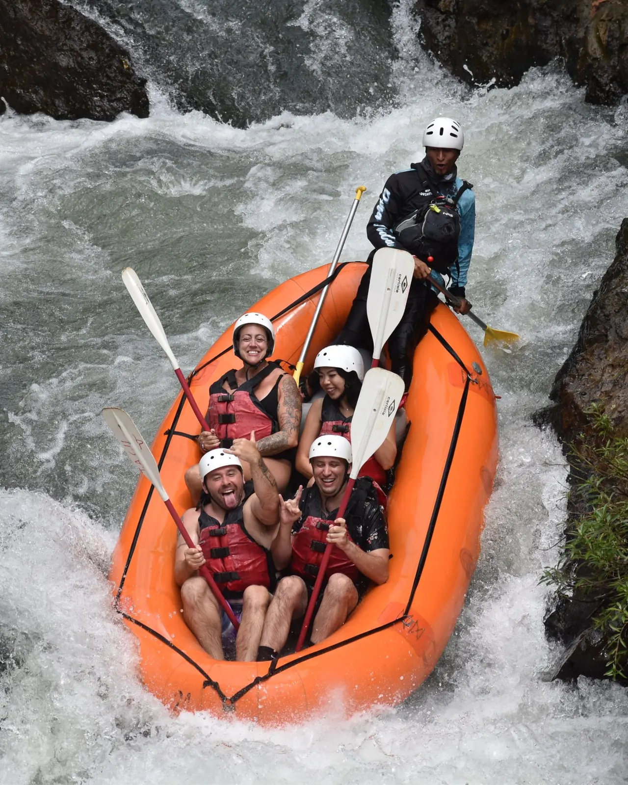 Guide and rafters in an orange raft dropping through whitewater rapids on the Tenorio River in Guanacaste